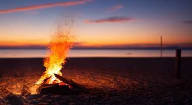 Yazın güzel bir plajın ortasında güzel bir kamp ateşi. Arka planda günbatımı ve güzel bir ışık var.