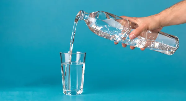 stock image person pouring water over a glass on blue background