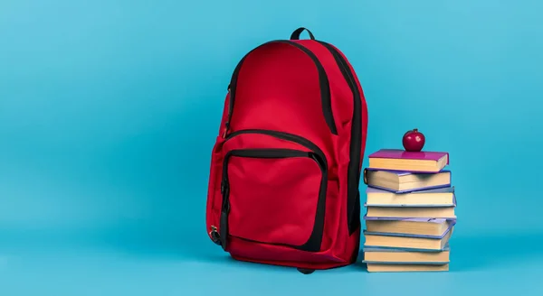 red school bag next to books with an apple on top