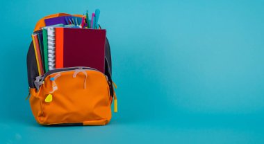 Mavi arka planda kitaplarla dolu turuncu okul çantası.
