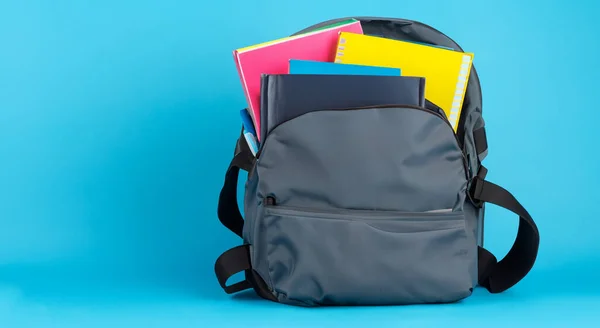 gray school bag full of books on blue background