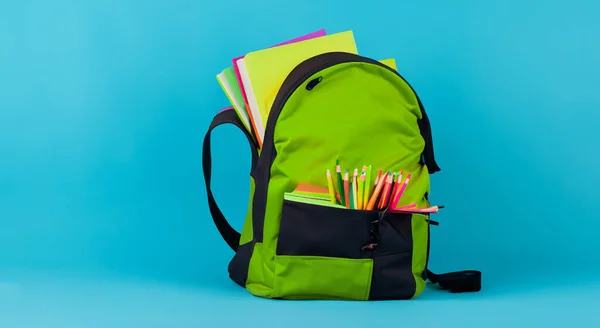 green school bag full of books on blue background HD