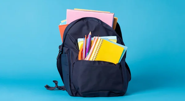 school bag with school books on blue background