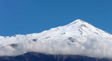 Mavi gökyüzü ve beyaz bulutlarla kaplı görkemli yüksek karla kaplı dağ