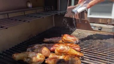 Bir adam açık havada ızgara yapar, tavuk budu ve domuz eti şeritlerini ızgarada pişirir. Cızırdayan et mükemmelliğe doğru pişerken zengin dumanlı lezzet için tuz ekler..
