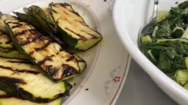 Tabakla dolu bir masayı tarayan bir video, içinde ızgara kabak izleri, taze salatalık salatası, ızgara domuz eti dilimleri ve ev yapımı ev yapımı ev yapımı bir yemek yakalayan sarımsaklı İsviçre pazarı..