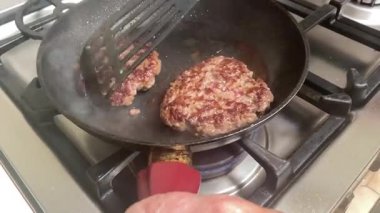 Yaşlı bir kadının, gaz aralığında tavada iki hamburger köftesi pişirirken, cızırdarken, ev yapımı konforlu gıdanın özünü yakalarken yakın plan çekimi..
