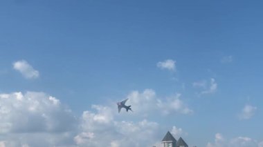 Canlı bir köpekbalığı şekilli uçurtma açık mavi gökyüzünde süzülerek güneşli bir günde rüzgarı yakalar. Pofuduk bulutlar arka planda süzülürken uçurtma sakin sahil evleriyle birlikte sakin bir sahil mahallesinde dans ediyor ve huzurlu ve neşeli bir manzara yaratıyor..