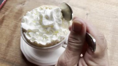 Beyaz kahve fincanının tepesinden krema temizlemek için küçük bir çay kaşığı kullanan bir adamın yakın çekim videosu, çay tabağıyla uyumlu bir fincan çay tabağıyla, ahşap bir masaya yerleştirilmiş..