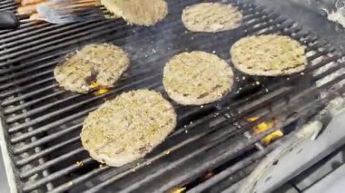 Tahta bir güvertede, gaz ızgarasında pişen bir adamın videosu. Güneşli bir yaz gününde, arka planda ağaçlar ve arka plan manzarası olan metal bir spatulayla hamburger çeviriyor..