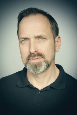 Stüdyoda siyah gömlekle ifade vermeye çalışan yaşlı bir adamın portresi.