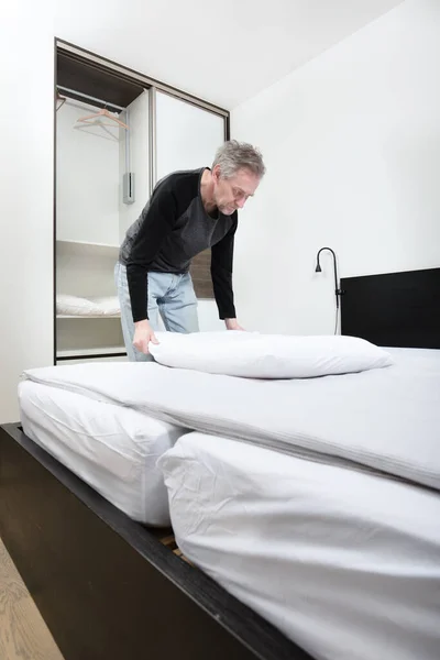 Older man working in bedroom on making bed