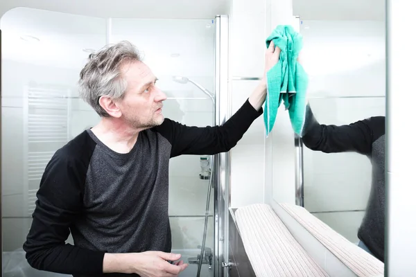 Older man cleaning bathroom space in apartment
