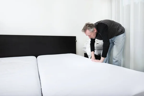 Older man working in bedroom on making bed