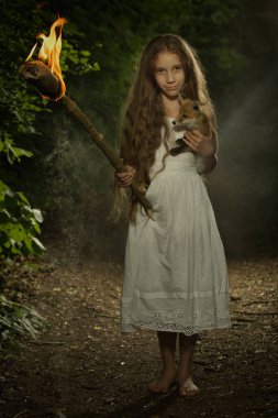 Karanlık ormanda poz veren hoş bir genç bayan alevler içinde bir meşaleyle