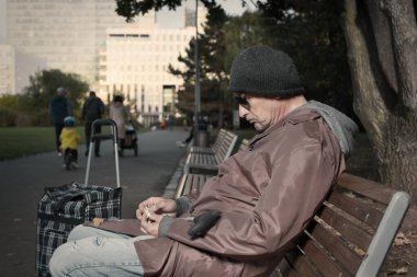 Yaşlı vatandaş şehir parkında tekerlekli arabayla yürüyor.