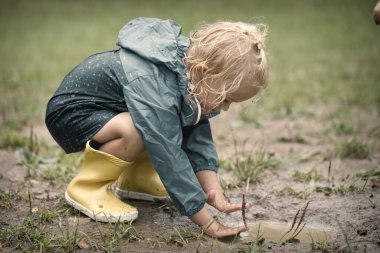 Çocuklar yağmurdan sonra çayırlarda yağmurluklarla oynuyorlar.
