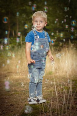 Kot giymiş küçük bir çocuk ormanda kütük ve patika üzerinde poz veriyor.