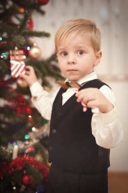 Noel günü resmi elbiseli bir çocuk ağacın yanındaki hediyeleri açıyor.