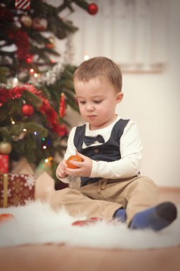 Küçük çocuk Noel günü ağacın yanında hediyeleri açıyor.