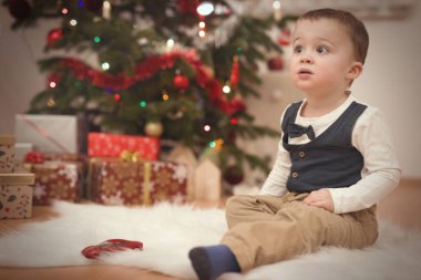 Küçük çocuk Noel günü ağacın yanında hediyeleri açıyor.