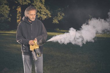 Yaşlı adam dışarıda iki çeşit duman makinesi jeneratörü kullanıyor.