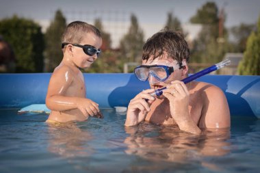 Couple of man and baby cooling during hot day in swimming pool on garden clipart