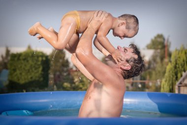 Couple of man and baby cooling during hot day in swimming pool on garden