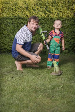 Little boy with father playing with power and garden tools on garden lawn clipart