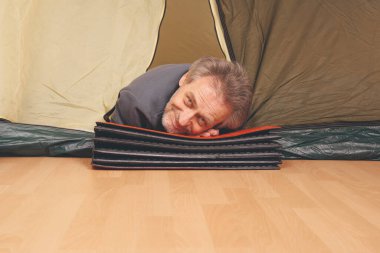 Yaşı büyük bir adam dışarıda kamp yapmak yerine apartman odasında çadır kuruyor.