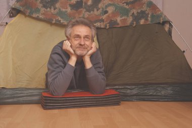 Yaşı büyük bir adam dışarıda kamp yapmak yerine apartman odasında çadır kuruyor.