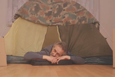 Yaşı büyük bir adam dışarıda kamp yapmak yerine apartman odasında çadır kuruyor.