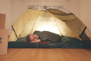 Yaşı büyük bir adam dışarıda kamp yapmak yerine apartman odasında çadır kuruyor.