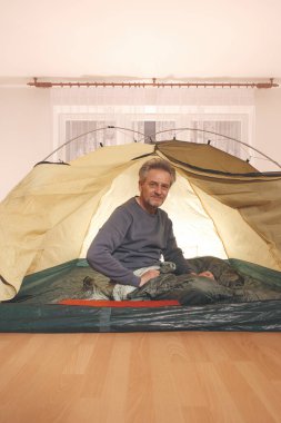 Yaşı büyük bir adam dışarıda kamp yapmak yerine apartman odasında çadır kuruyor.