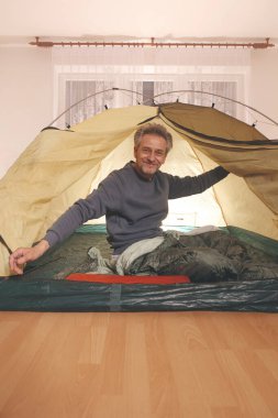 Yaşı büyük bir adam dışarıda kamp yapmak yerine apartman odasında çadır kuruyor.