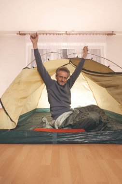 Yaşı büyük bir adam dışarıda kamp yapmak yerine apartman odasında çadır kuruyor.