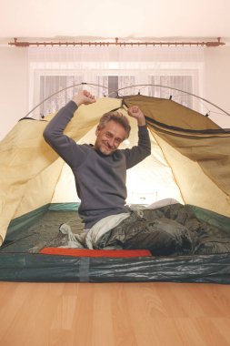 Yaşı büyük bir adam dışarıda kamp yapmak yerine apartman odasında çadır kuruyor.