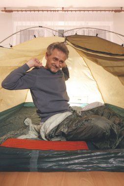 Yaşı büyük bir adam dışarıda kamp yapmak yerine apartman odasında çadır kuruyor.