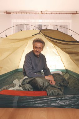 Yaşı büyük bir adam dışarıda kamp yapmak yerine apartman odasında çadır kuruyor.