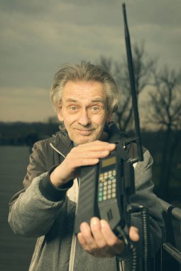 Köprüde yaşlı bir adam eski cep telefonuyla arıyor.