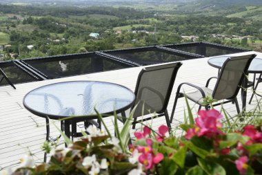 Masalar ve terasta demir sandalyeler. Çiçek saksıları ve manzara manzaralı.