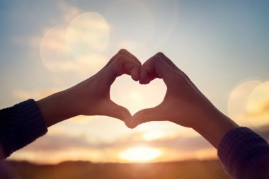 Gün batımında gökyüzü arka planında çocuk eli olan kalp şekli