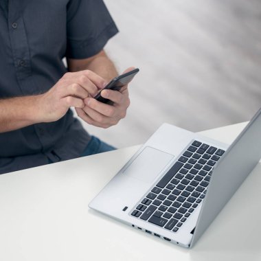 Akıllı cep telefonu ve yüksek açılı dizüstü bilgisayar kullanan bir iş adamı