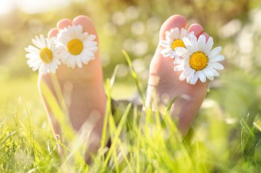 Ayak parmaklarının arasında papatya çiçekleri olan çocuk yaz güneşinde çayırda dinleniyor.