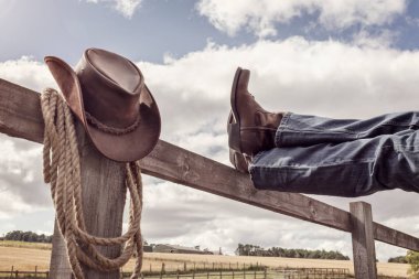 Kovboy çizmeleri ve ayaklı şapka çiftlikteki çitlerin üzerinde bacak bacak bacak üstüne atmış, country müzik festivali konser veya çizgi dansı konsepti