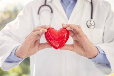 Klinikte ya da sağlık hizmetleri ve sağlıklı yaşam tarzında hastane konseptinde kırmızı kalp tutan doktor ya da kardiyolog
