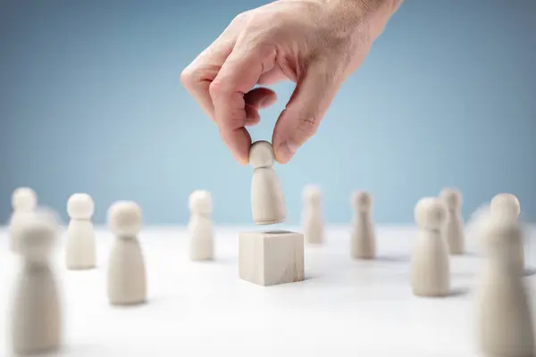 stock image Leadership, help and assistance concept, wooden business team with one person standing out from the crowd being placed on podium by hand