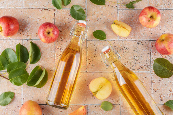 Apple cider vinegar of fermented fruit into a two glass bottles with fresh organic ripe red apples on beige concrete background. Vitamin superfood drink, Healthy eating lifestyle, top view, flat lay