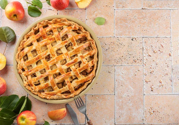 Homemade Apple Pie with fresh red apple and leaves on beige travertine tiles table background, top view, flat lay Classic autumn Thanksgiving dessert apple pie, copy space