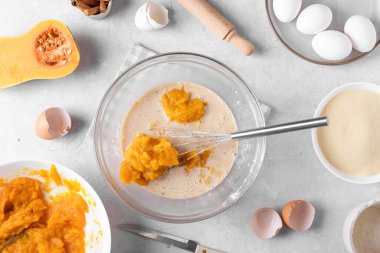 Mutfaktaki gri bir masada turta pişirmek için kabak turtası ve malzemelerle dolu bir kase. Ev yemeği konsepti, geleneksel Şükran Günü balkabağı turtası tarifi, üst manzara, düz yatak